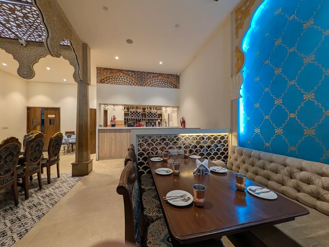 Wooden dining tables with cushioned banquette seating and a blue jali wall